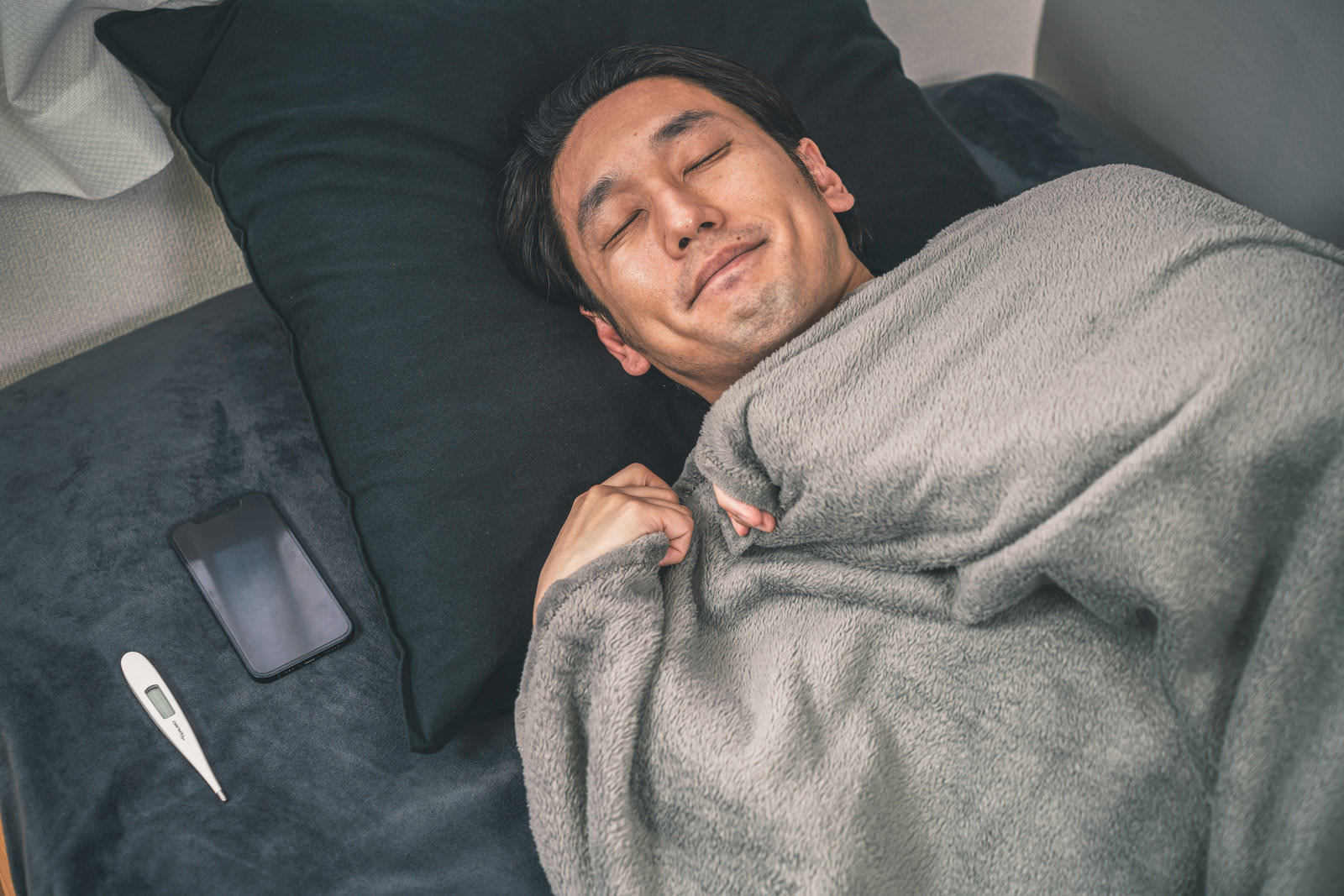 枕元にスマホを置いて眠る日本人男性